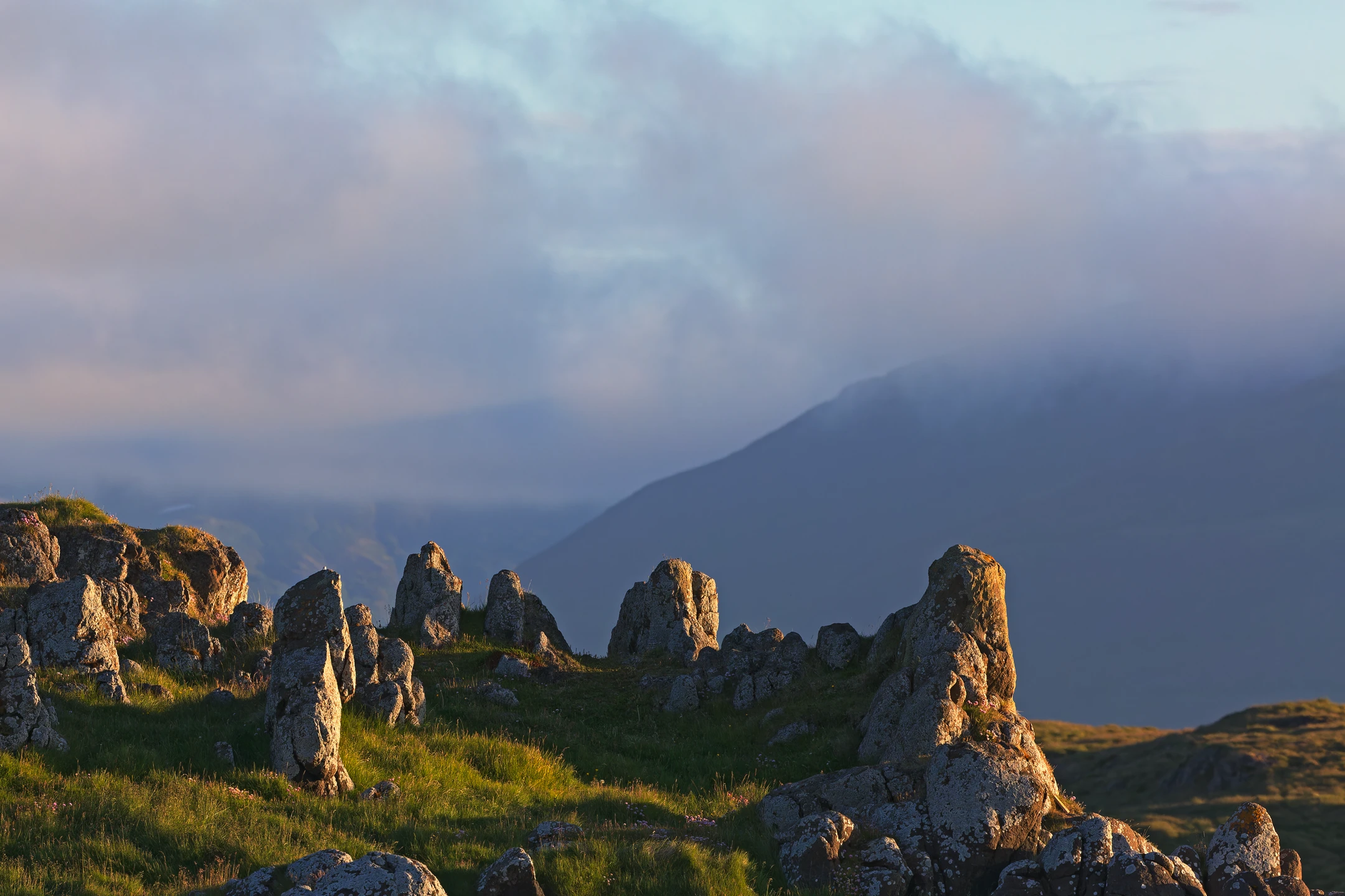 Photo : Mégalithes naturels et montagnes baignées d'une lumière rasante.